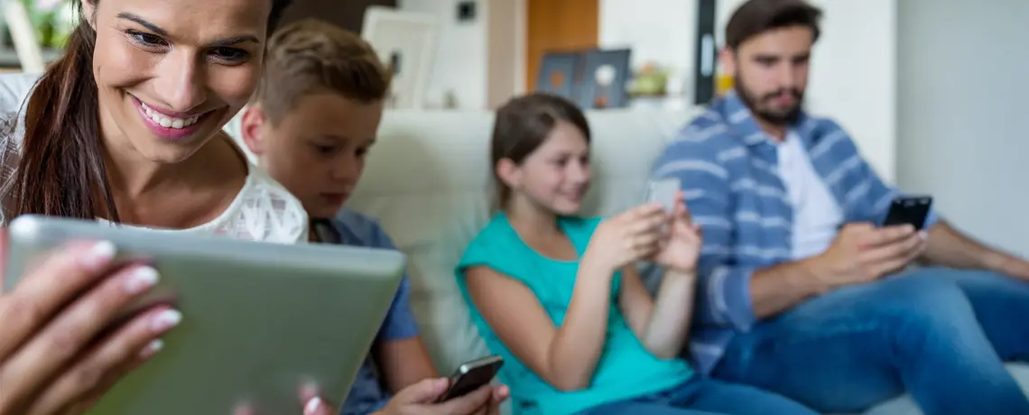 Eine 4 köpfige Familie sitzt im Wohnzimmer auf der Couch und alle haben ein mobiles Endgerät in der Hand